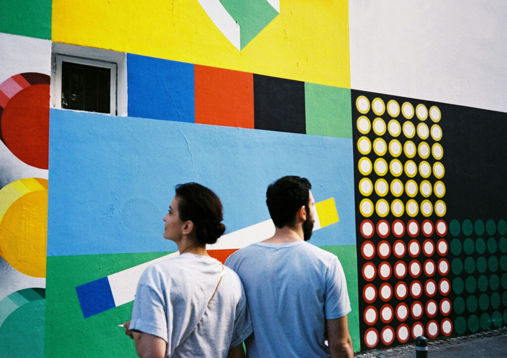 A couple stands in front of a colourful painted wall