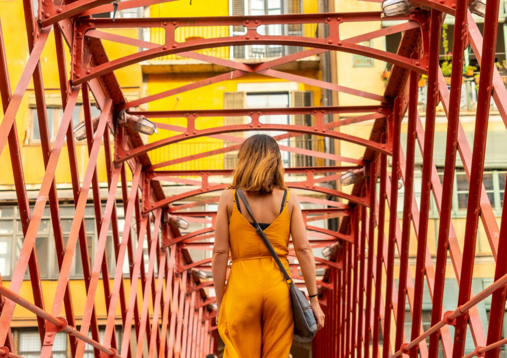 Young tourist dress in orange walking on a red metal bridge