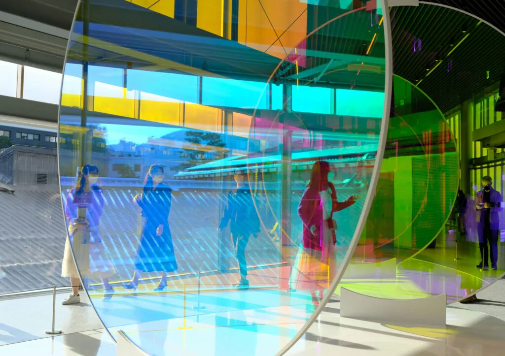 A group of people standing inside a building walking among coloured glass