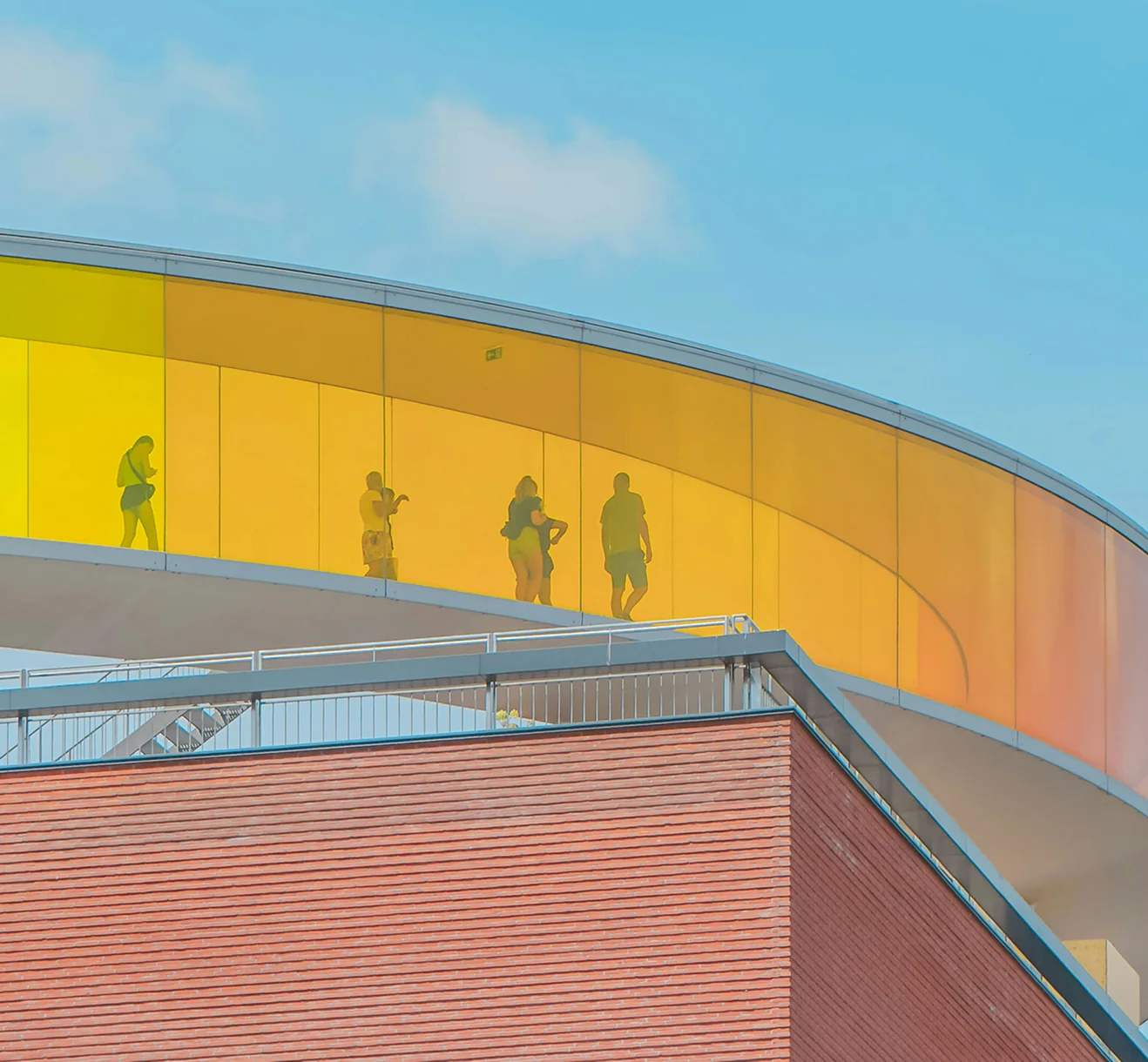 View from below of a colourful yellow glass building on a bright blue sky background